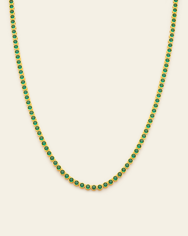 A Gold Vermeil bezel set tennis necklace with emerald green CZ stones and an open box clasp displayed on a cream background.