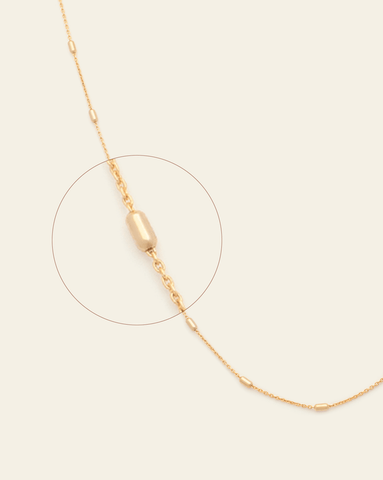 A magnified image of Gold Vermeil rolo chain spaced between barrel beaded links on a cream background.