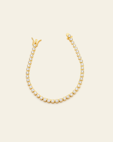 A Gold Vermeil bezel set tennis bracelet with CZ stones and an open box clasp displayed on a cream background.