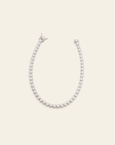 Sterling silver tennis bracelet featuring bezel-set sparkling cubic zirconia stones on a cream background.