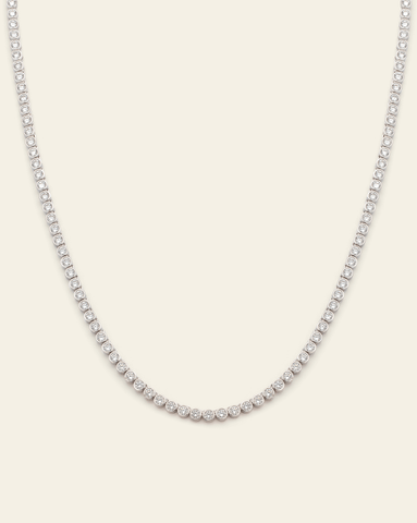 Sterling silver tennis necklace featuring bezel-set sparkling cubic zirconia stones on a cream background.