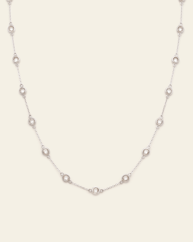 A photo of a bezel station chain necklace in Sterling Silver featuring multiple small, round CZ stones evenly spaced along the delicate chain, against a cream background.