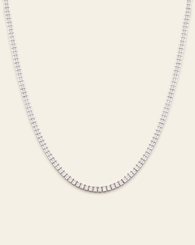 Sterling silver tennis necklace featuring bezel-set sparkling cubic zirconia stones on a cream background.