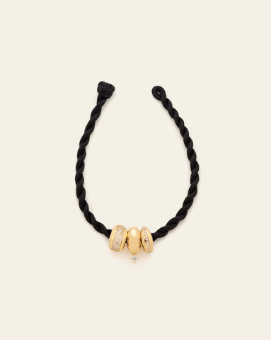 Black twisted cord bracelet with three gold bead charms, two adorned with pavé CZ stones and one featuring a small dangling stone, displayed against a neutral background.