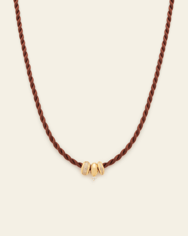 Brown twisted cord necklace with three gold bead charms, two adorned with pavé CZ stones and one featuring a small dangling CZ stone, displayed against a neutral background.