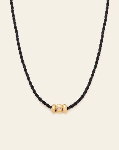 Black twisted cord necklace with three gold bead charms, one adorned with small diamonds, set against a neutral background.