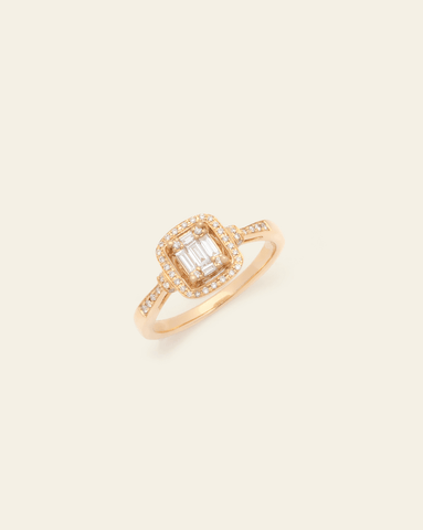 A 14k Yellow Gold cushion-shaped diamond ring featuring a central cluster of baguette diamonds surrounded by a halo of smaller diamonds, and a row of smaller round diamonds along the band on a cream background. 