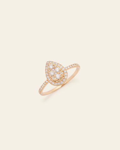 A 14k Yellow Gold teardrop-shaped diamond ring featuring a cluster of diamonds and a row of smaller round diamonds along the band on a cream background. 