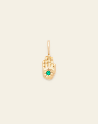 A photo of a Gold Vermeil pendant in the shape of a hand with a small green CZ stone set in the center of the palm on a cream background.