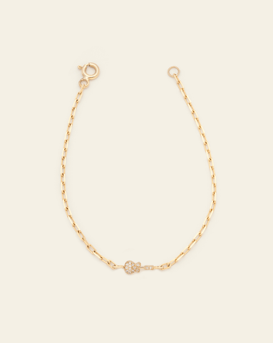 A photo of a Solid Yellow Gold thin staple chain bracelet with a pave White Topaz guitar charm in the centre against a cream background. 