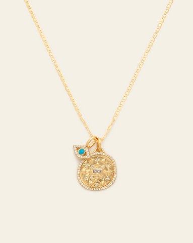 A Gold Vermeil necklace with a round medallion pendant featuring geometric patterns with CZ stones with an evil eye charm with a turquoise stone in the centre, set against a cream background.