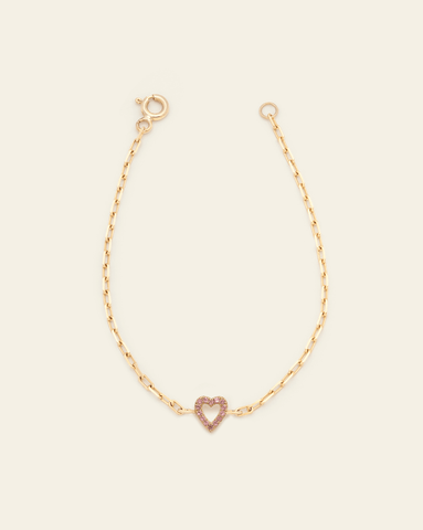 A photo of a Solid Yellow Gold thin staple chain bracelet with an open heart pave Pink Tourmaline charm in the centre against a cream background. 