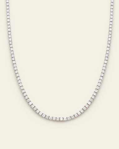 A photo of a Sterling Silver tennis necklace featuring prong-set sparkling cubic zirconia stones on a cream background.