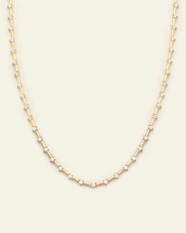 A photo of a Gold Vermeil tennis necklace with clear CZ stones spaced out by gold tabs, displayed against a cream background. 