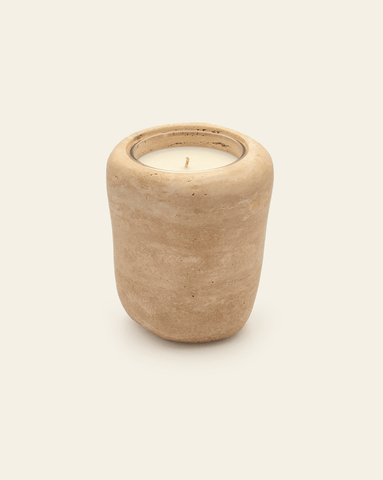 A photo of a beige travertine stone candle holder with an organic, rounded shape, holding a candle against a cream background. 