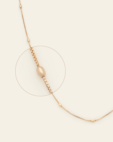 A magnified image of Gold Vermeil box chain spaced between oval beaded links on a cream background.