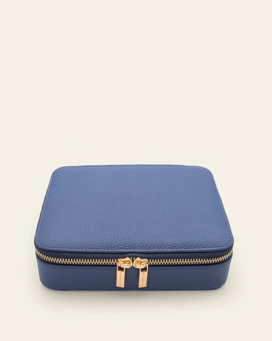 Animated image of a cobalt blue oversized jewelry case with gold zippers, shown opening to reveal multiple compartments and slots for organizing various jewelry pieces.