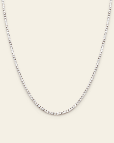 Sterling silver tennis necklace featuring prong-set sparkling cubic zirconia stones on a cream background.