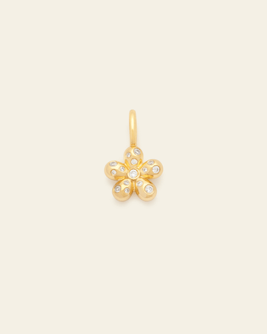 Gold vermeil pendant in the shape of a puffed flower, adorned with multiple small cubic zirconia stones on a cream background.