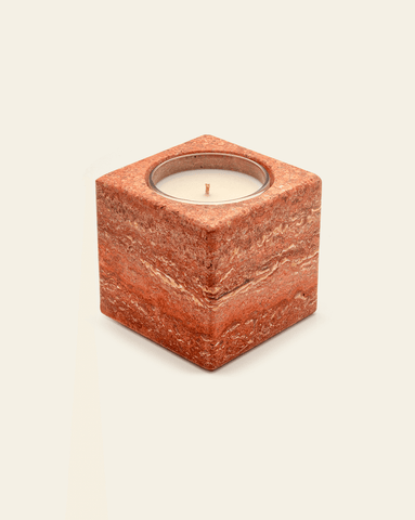 A photo of a square shaped red travertine stone candle holder, holding a candle against a cream background.