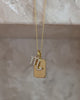 A close up video of a Gold Vermeil necklace with a delicate cable chain, featuring two charms: a small rectangular tag and a pave CZ Scorpio zodiac charm, set against a marbled background. 