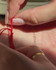 A close up video of a model showing how to loosen a red woven thread bracelet by pulling on one end of the bracelet to expand it for removal.